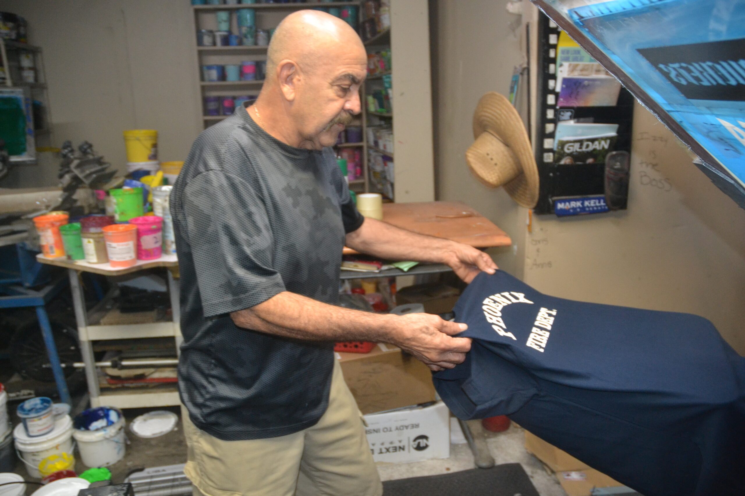 Owner of Phoenix Custom Tees holding a navy firefighter shirt inside the print shop.